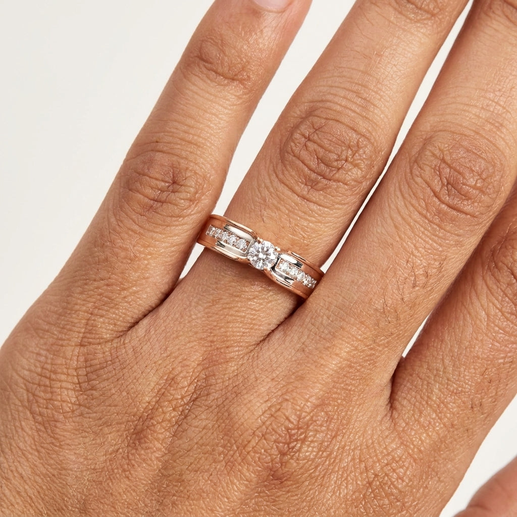 A solitaire diamond ring with a combination of white and rose gold, featuring a central diamond surrounded by smaller side diamonds on the band is worn in a hand's finger.