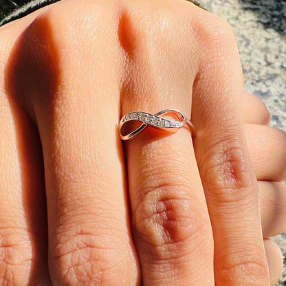 A person's hand displaying a 14K gold diamond band ring with a infinity shaped inset showing the diamond's cut and color.