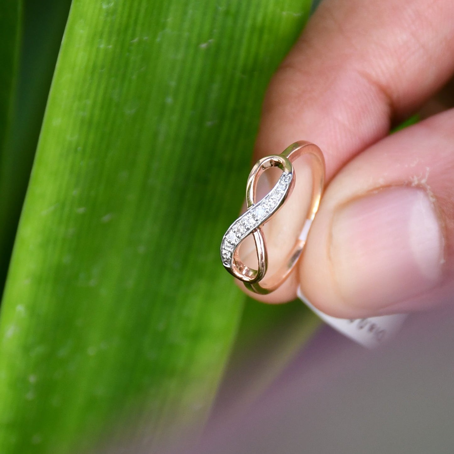 A person's hand displaying a 14K gold diamond band ring with a infinity shaped inset showing the diamond's cut and color.