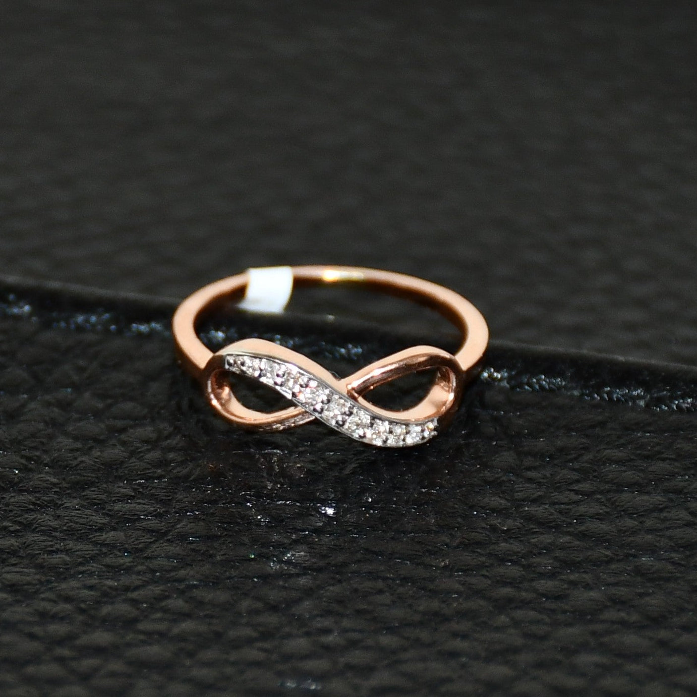 A 14K gold diamond band ring with a infinity shaped inset showing the diamond's cut and color, displayed on a black leather surface.