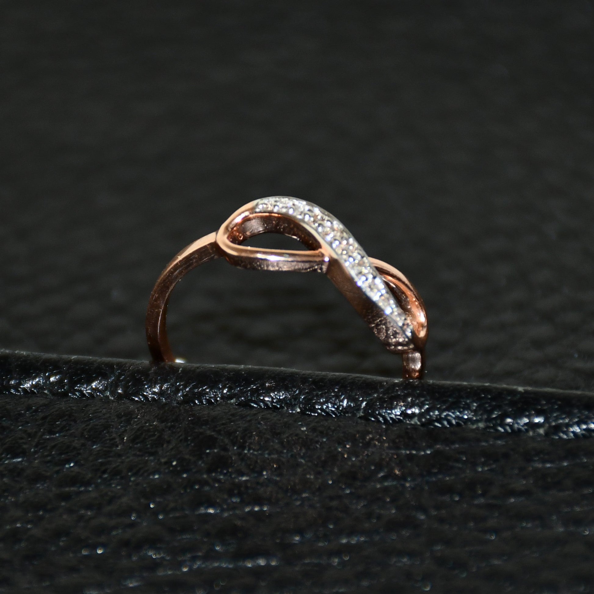 A 14K gold diamond band ring with a infinity shaped inset showing the diamond's cut and color, displayed on a black leather surface.