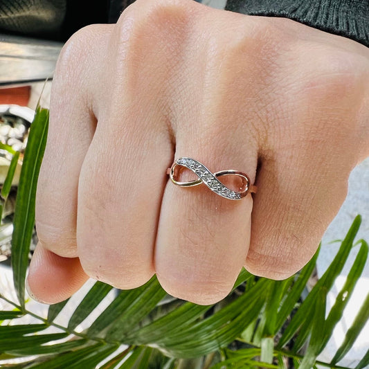 A person's hand displaying a 14K gold diamond band ring with a infinity shaped inset showing the diamond's cut and color.