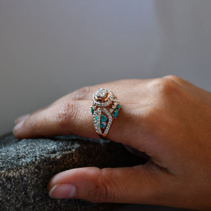 A woman's hand on a rock stone displaying a rose gold diamond ring with a central brilliant cut diamonds and smaller color stones around it.