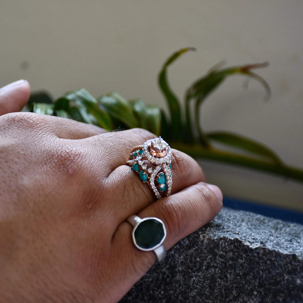 A woman's hand on a rock stone displaying a rose gold diamond ring with a central brilliant cut diamonds and smaller color stones around it.