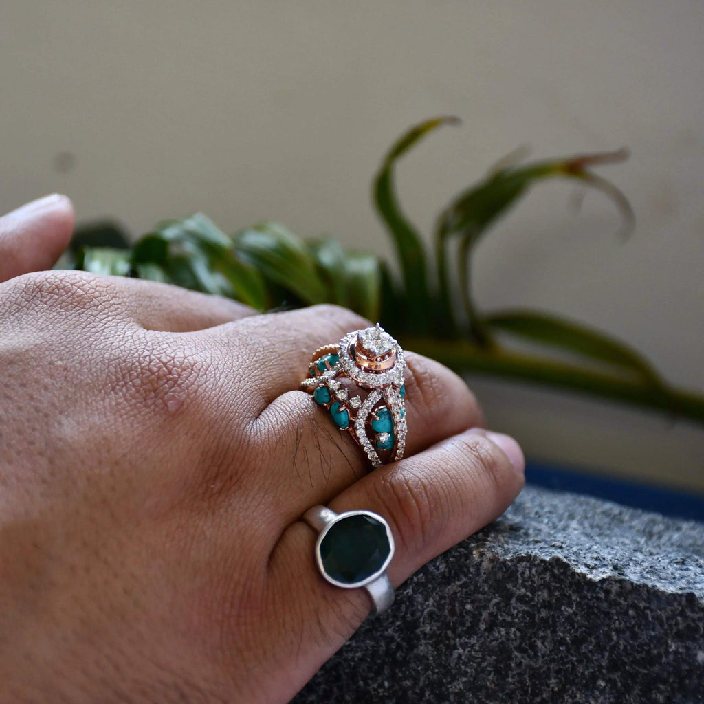 A woman's hand on a rock stone displaying a rose gold diamond ring with a central brilliant cut diamonds and smaller color stones around it.