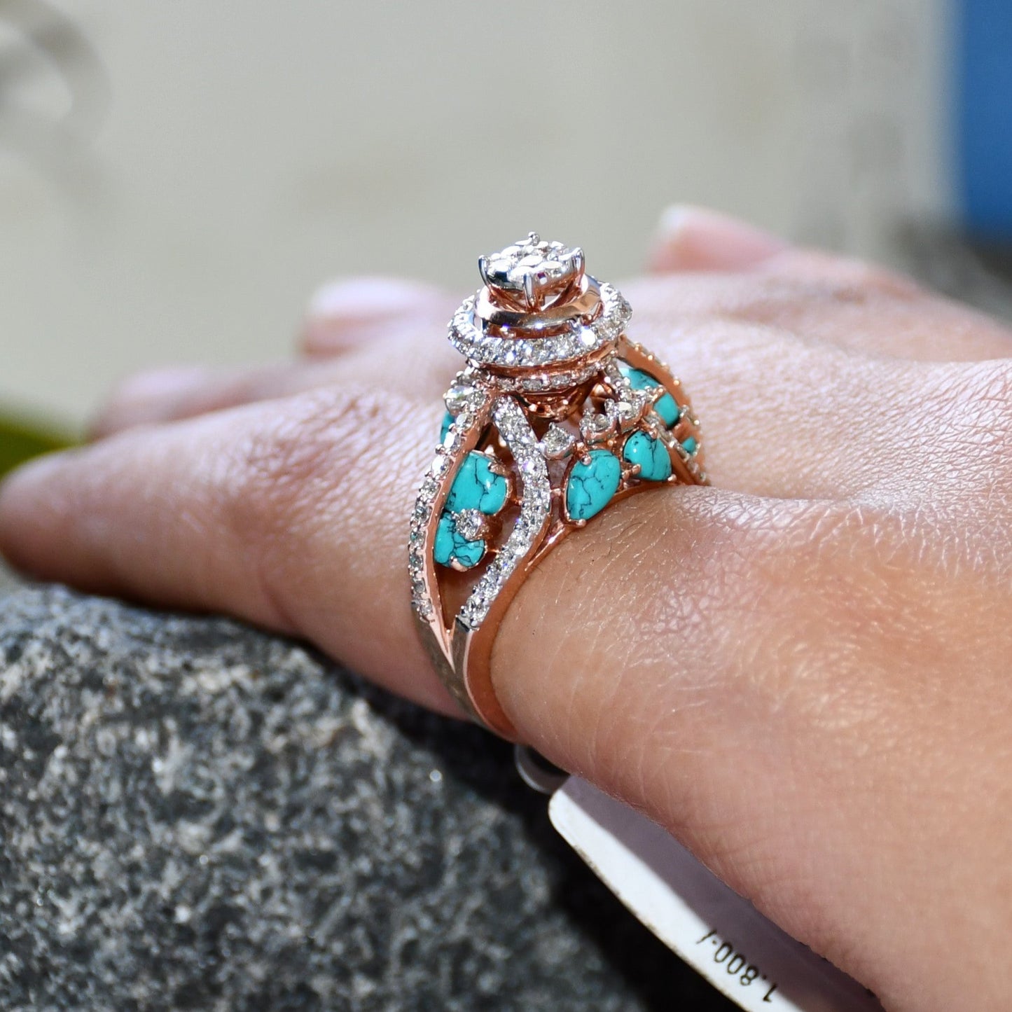 A woman's hand displaying a rose gold diamond ring with a central brilliant cut diamonds and smaller color stones around it.