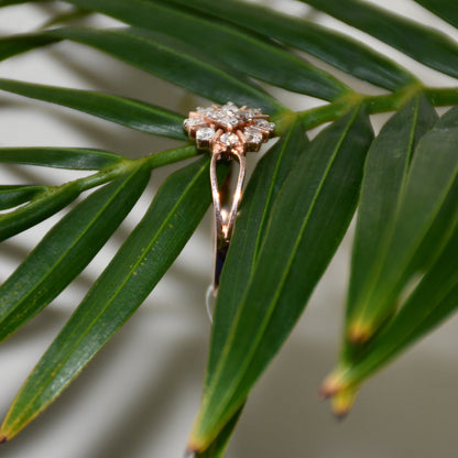 A 14kt gold band ring with a round brilliant cut diamond centerpiece, set on a leafy background.