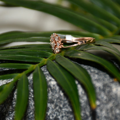 A 14kt gold band ring with a round brilliant cut diamond centerpiece, set on a leafy and rough surface.