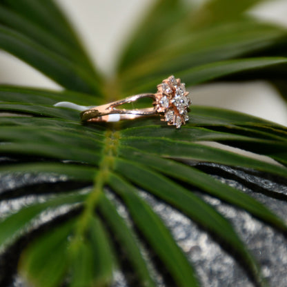 A 14kt gold band ring with a round brilliant cut diamond centerpiece, set on a leafy and rough surface.