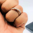 A person's hand holding a diamond band ring with 14K gold hallmark, beside a mobile phone.