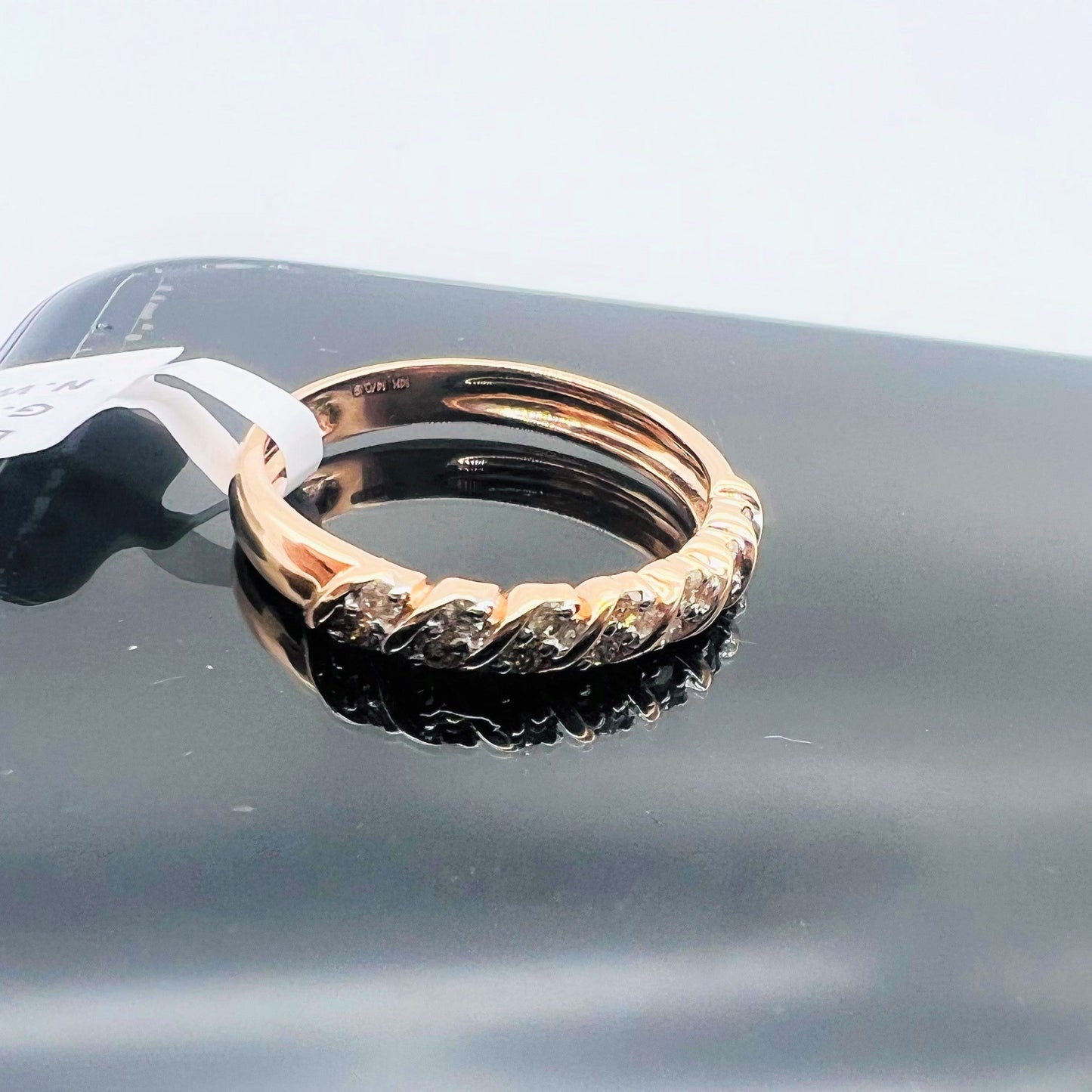 A 14K gold hallmark ring with certified diamonds set around its circumference is displayed on a reflective surface.