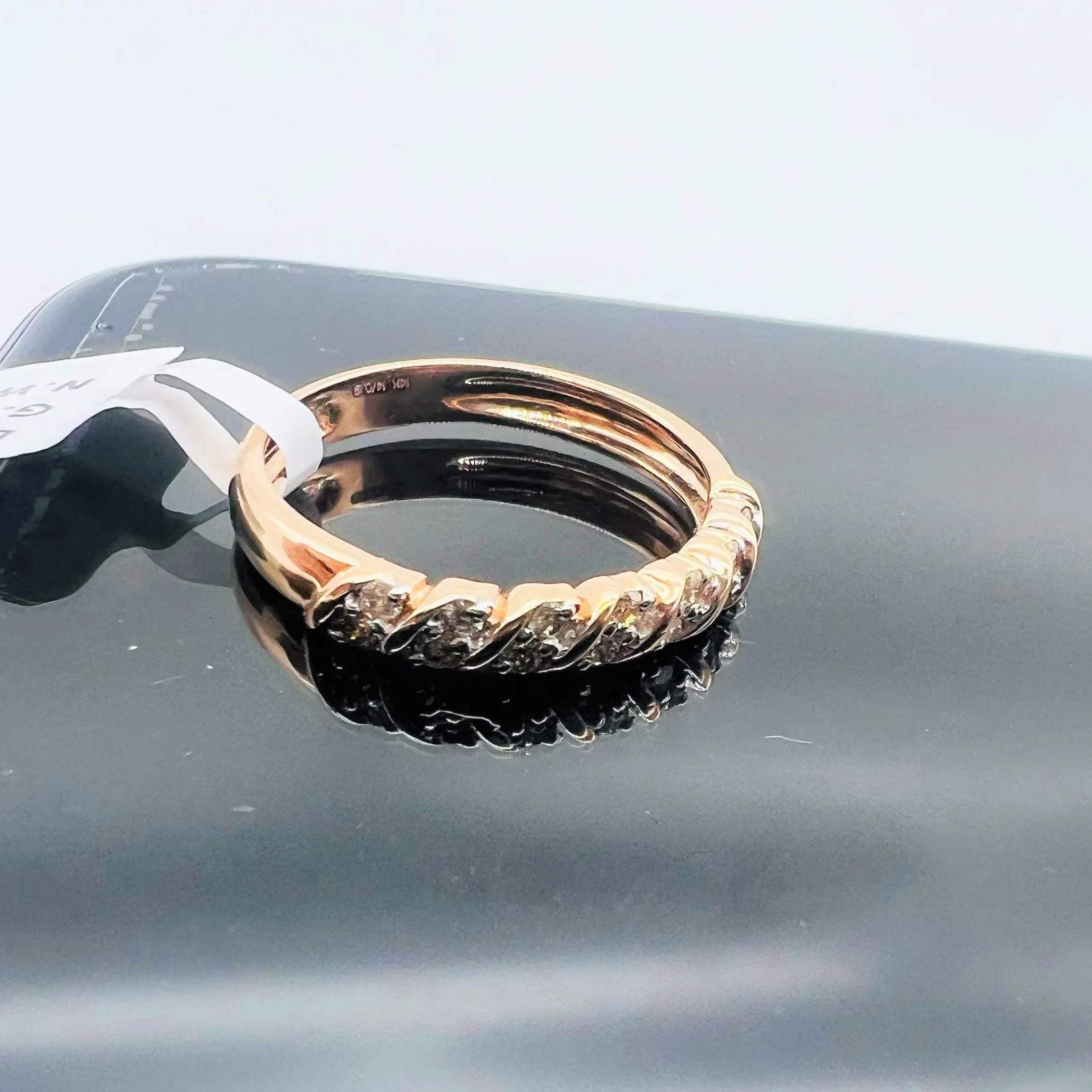A 14K gold hallmark ring with certified diamonds set around its circumference is displayed on a reflective surface.