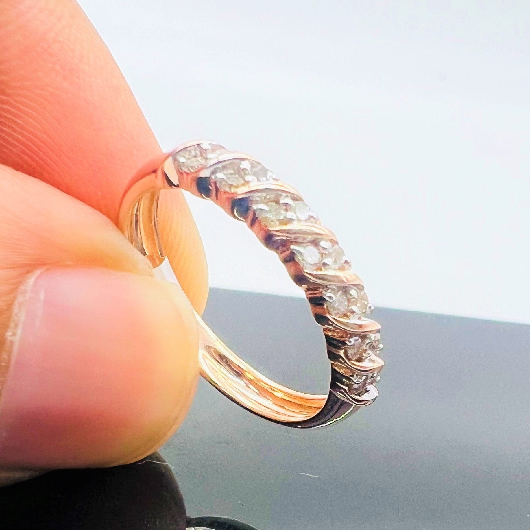 A person's hand holding a 14K gold hallmark ring with certified diamonds set around its circumference.