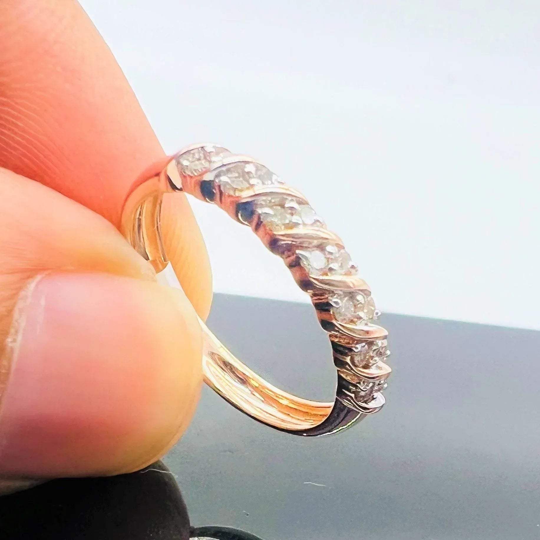 A person's hand holding a 14K gold hallmark ring with certified diamonds set around its circumference.