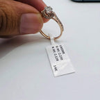 A 14kt gold hallmarked diamond band ring with a brilliant cut diamond centerpiece, held between fingers.