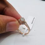 A 14kt gold hallmarked diamond band ring with a brilliant cut diamond centerpiece, held between fingers.