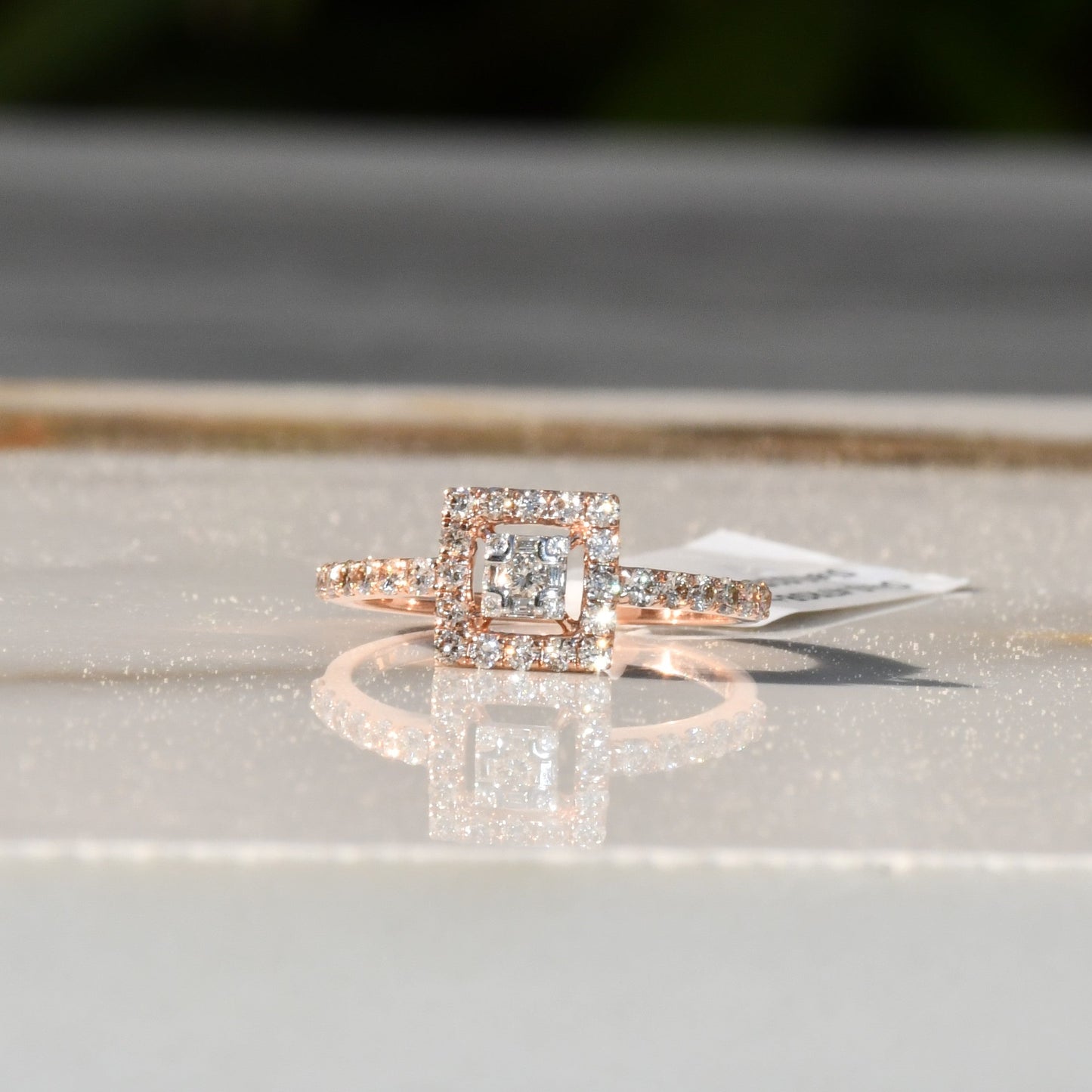 A 14K gold ring with a central square-shaped setting holding a sparkling, multicolored diamond, surrounded by smaller round diamonds set in a polished, reflective surface.