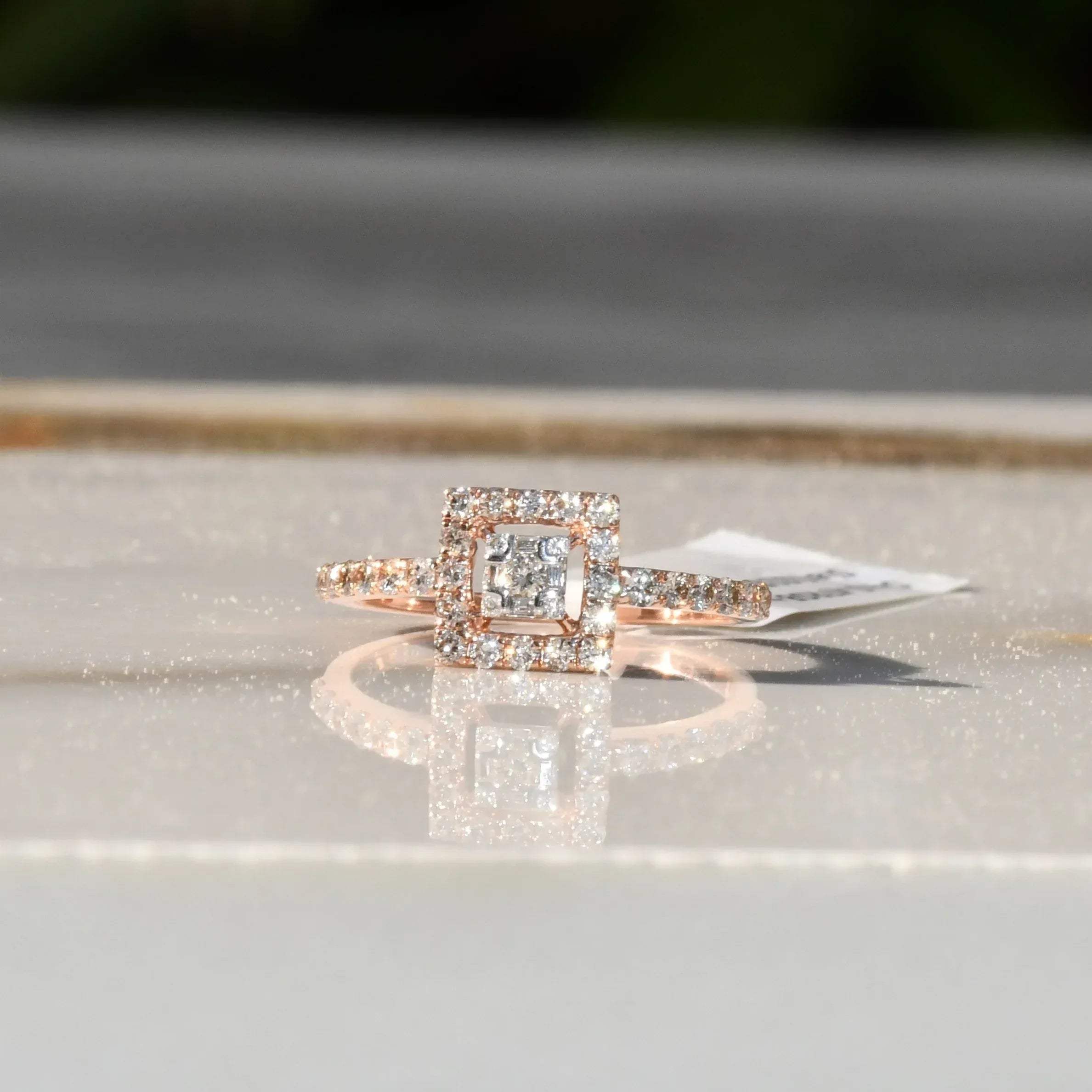 A 14K gold ring with a central square-shaped setting holding a sparkling, multicolored diamond, surrounded by smaller round diamonds set in a polished, reflective surface.