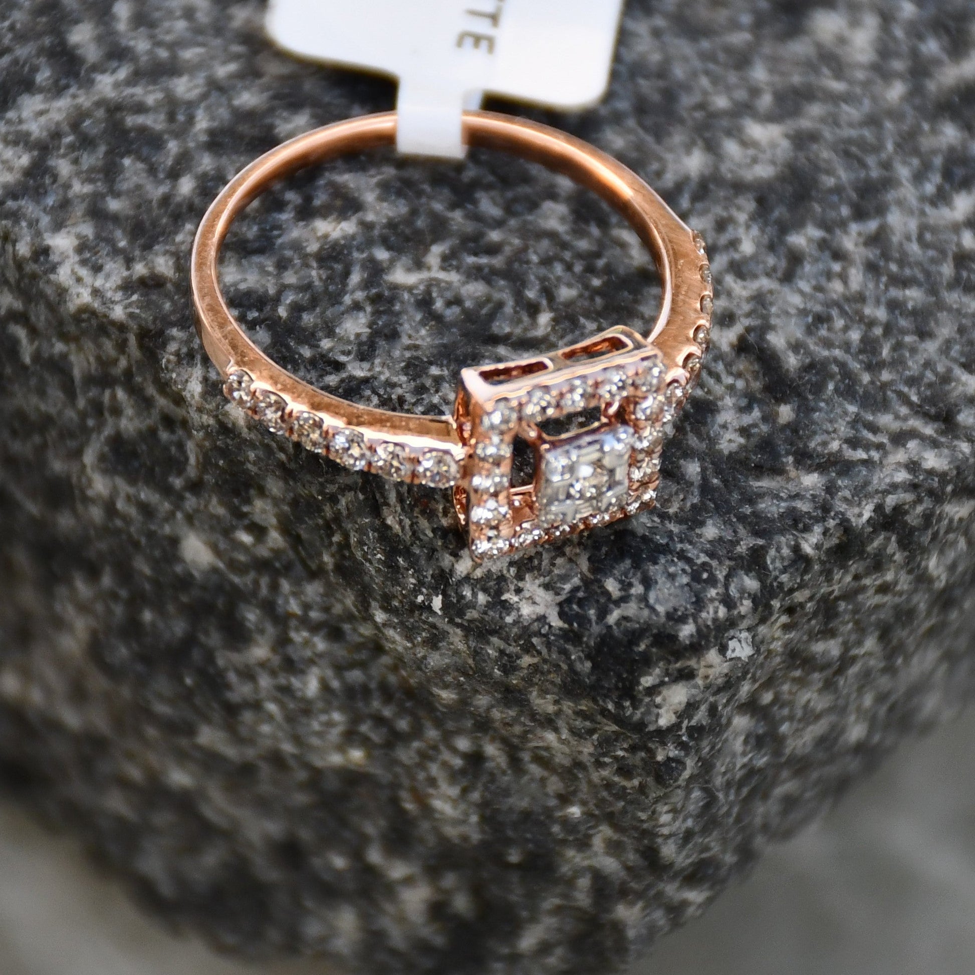 A 14K gold ring with a central square-shaped setting holding a sparkling, multicolored diamond, surrounded by smaller round diamonds set in a rough and textured surface.