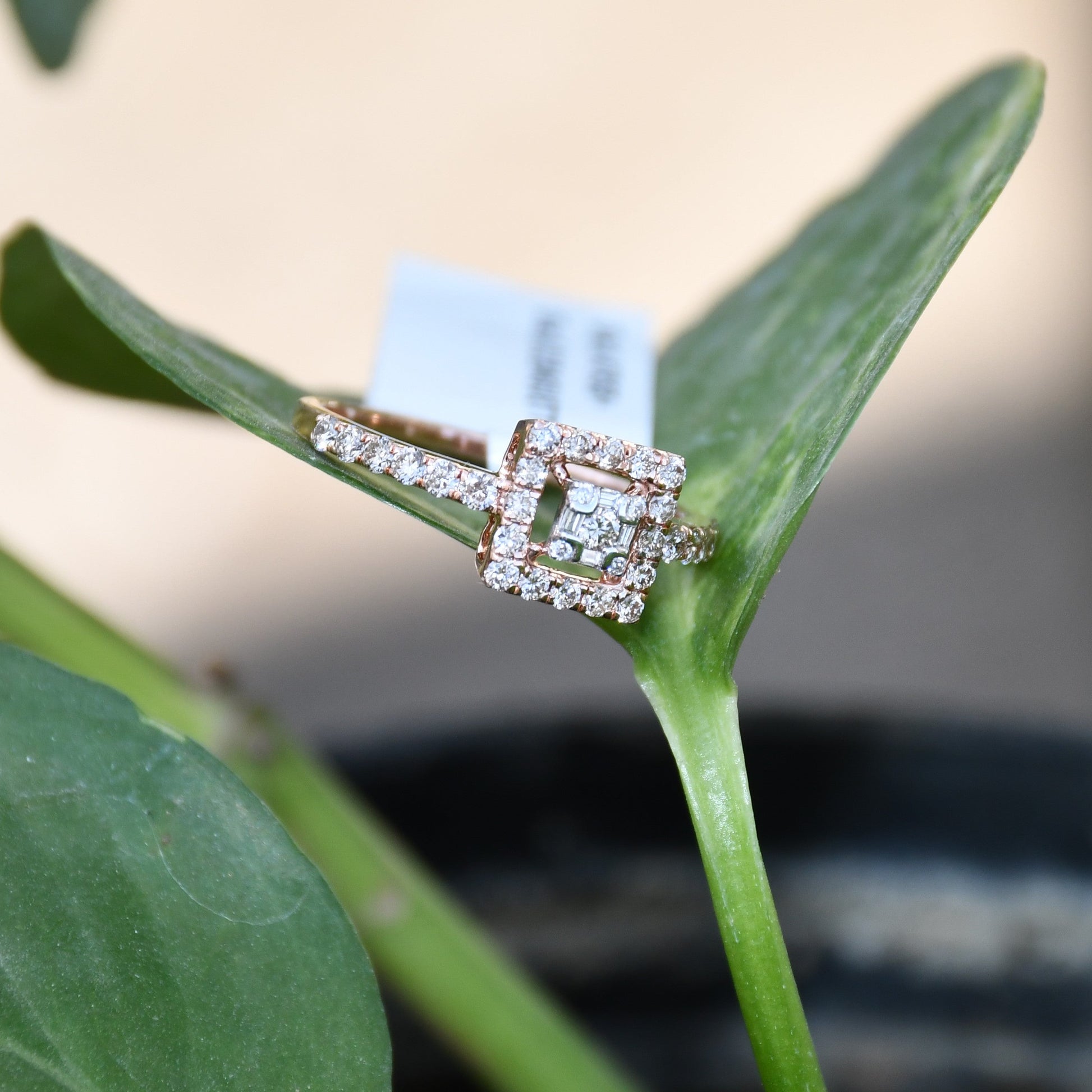 A 14K gold ring with a central square-shaped setting holding a sparkling, multicolored diamond, surrounded by smaller round diamonds set on a green leaf.