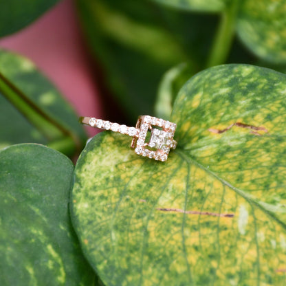 A 14K gold ring with a central square-shaped setting holding a sparkling, multicolored diamond, surrounded by smaller round diamonds set on a green leaf.