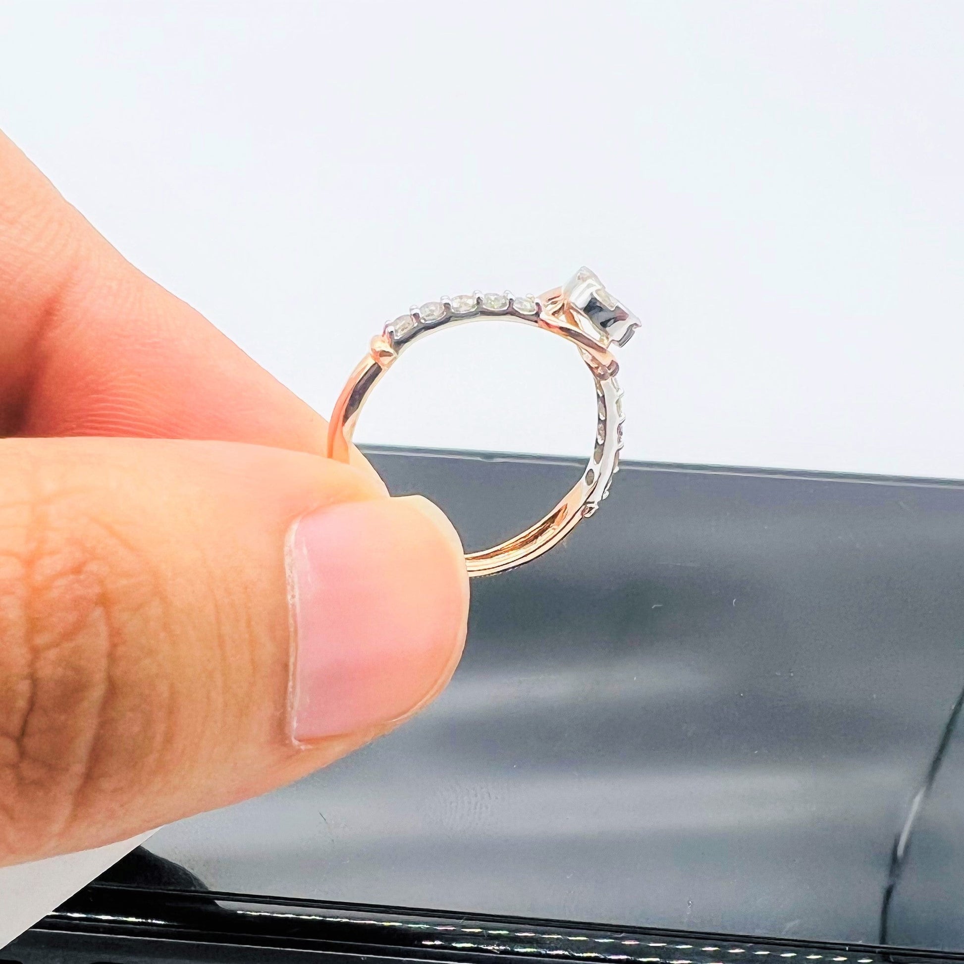 Hand holding a gold ring with a pear-shaped diamond center stone and a band adorned with small round diamonds.