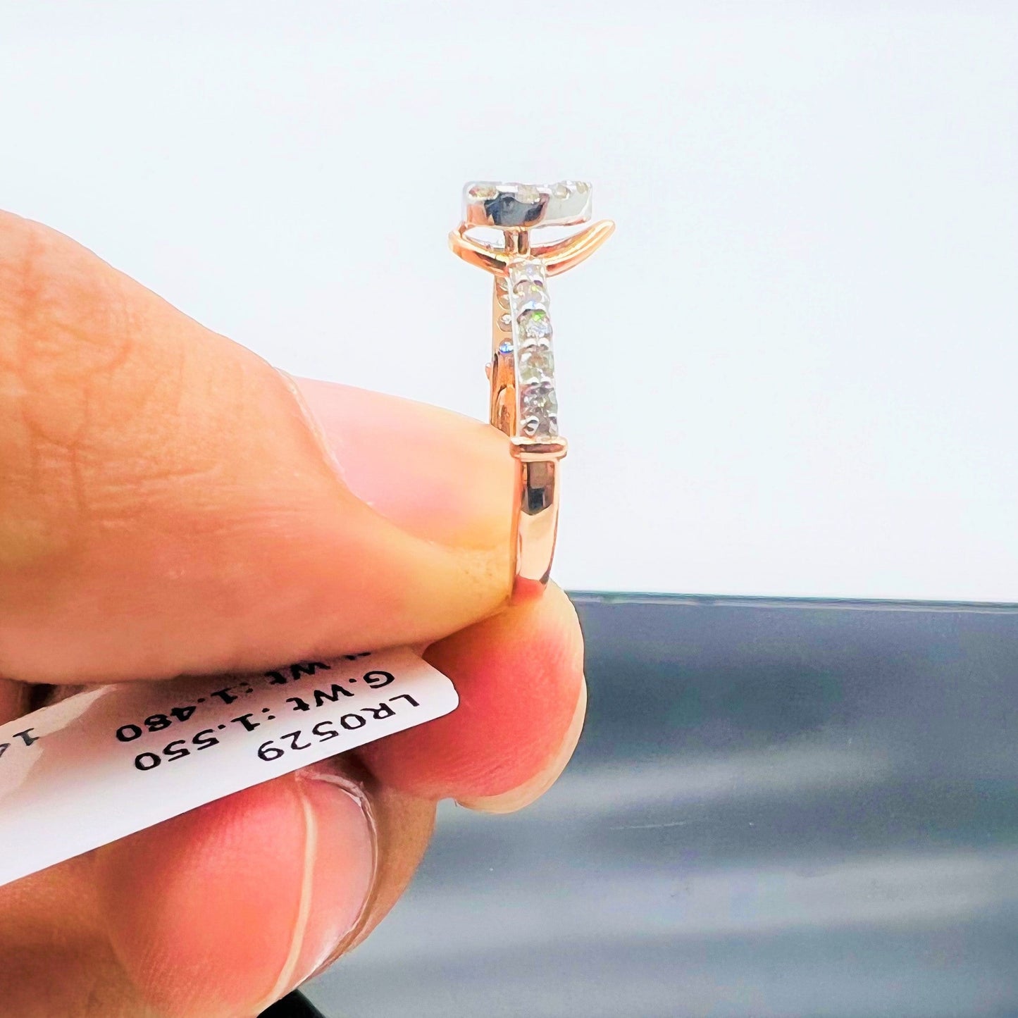 Hand holding a gold ring with a pear-shaped diamond center stone and a band adorned with small round diamonds with its details tag.