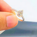 Hand holding a gold ring with a pear-shaped diamond center stone and a band adorned with small round diamonds.