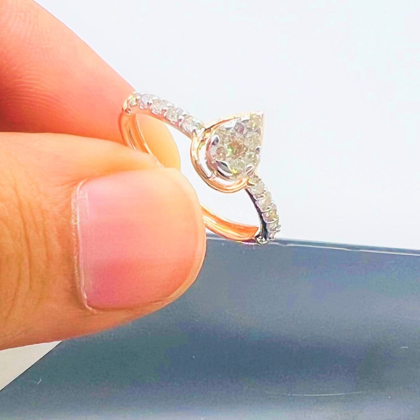 Hand holding a gold ring with a pear-shaped diamond center stone and a band adorned with small round diamonds.