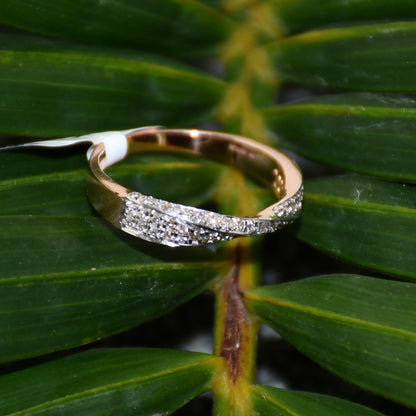 Elegant two-tone diamond ring featuring intertwined bands of rose gold and white gold, adorned with small round-cut diamonds, displayed on a green leaf.