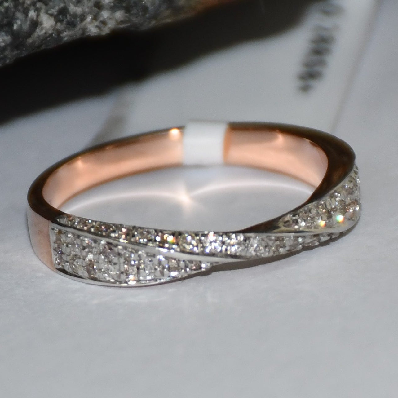 Elegant two-tone diamond ring featuring intertwined bands of rose gold and white gold, adorned with small round-cut diamonds, displayed on a white paper.