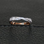 Elegant two-tone diamond ring featuring intertwined bands of rose gold and white gold, adorned with small round-cut diamonds, displayed on black leather background.