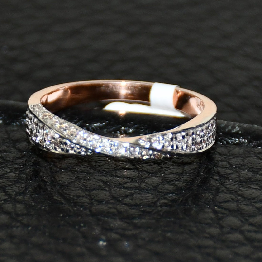 Elegant two-tone diamond ring featuring intertwined bands of rose gold and white gold, adorned with small round-cut diamonds, displayed on black leather background.