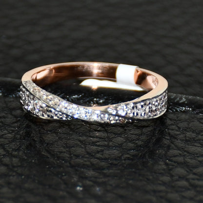 Elegant two-tone diamond ring featuring intertwined bands of rose gold and white gold, adorned with small round-cut diamonds, displayed on black leather background.