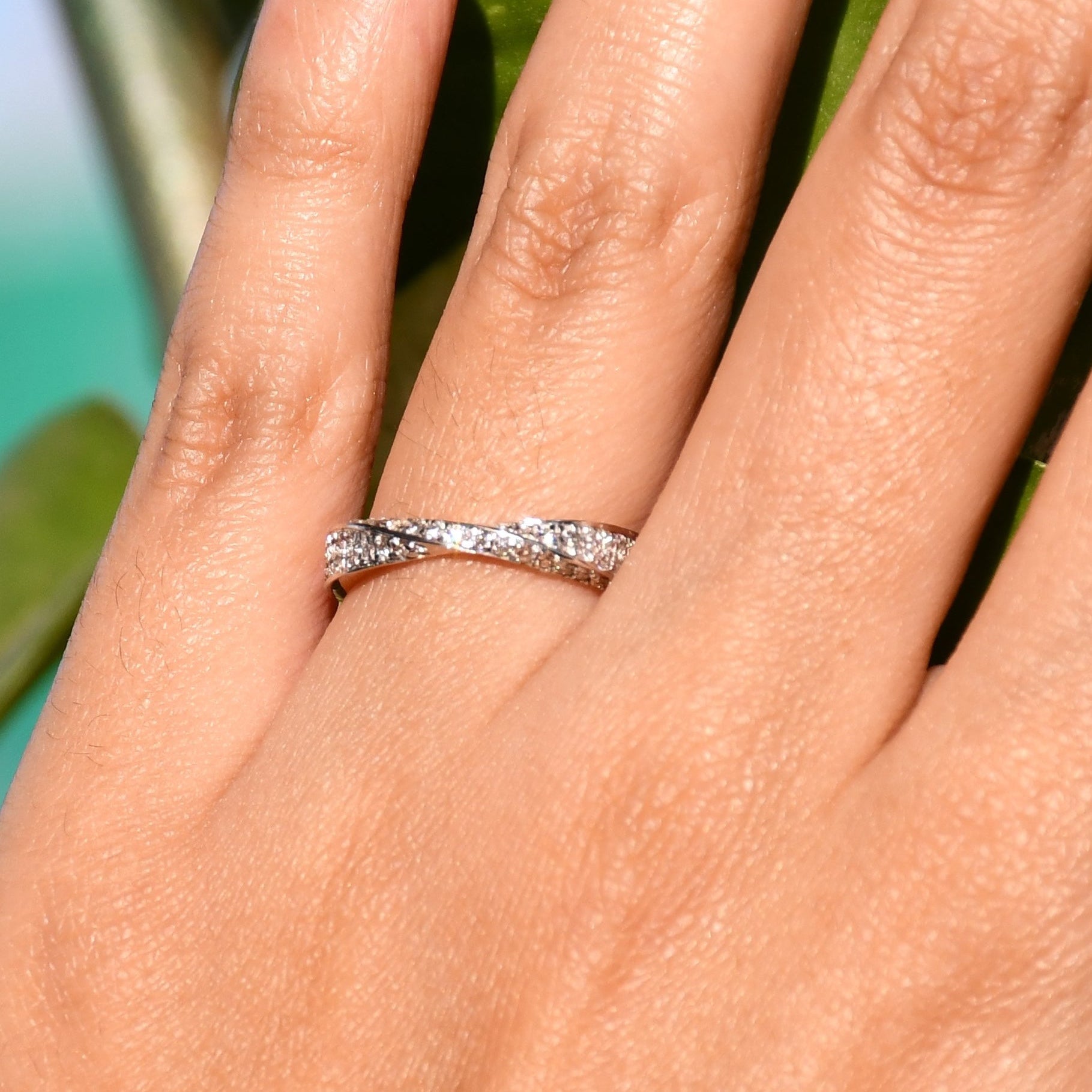 Elegant two-tone diamond ring featuring intertwined bands of rose gold and white gold, adorned with small round-cut diamonds, displayed worn in a hand's finger.