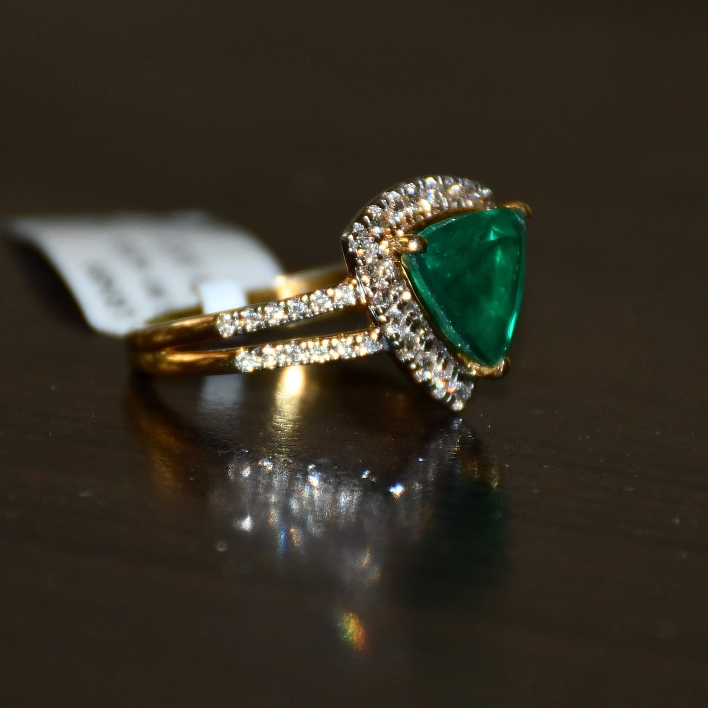 A green semi-precious stone ring with a 14KT gold band and brilliant cut diamonds on the top and bottom is displayed on a reflective surface.