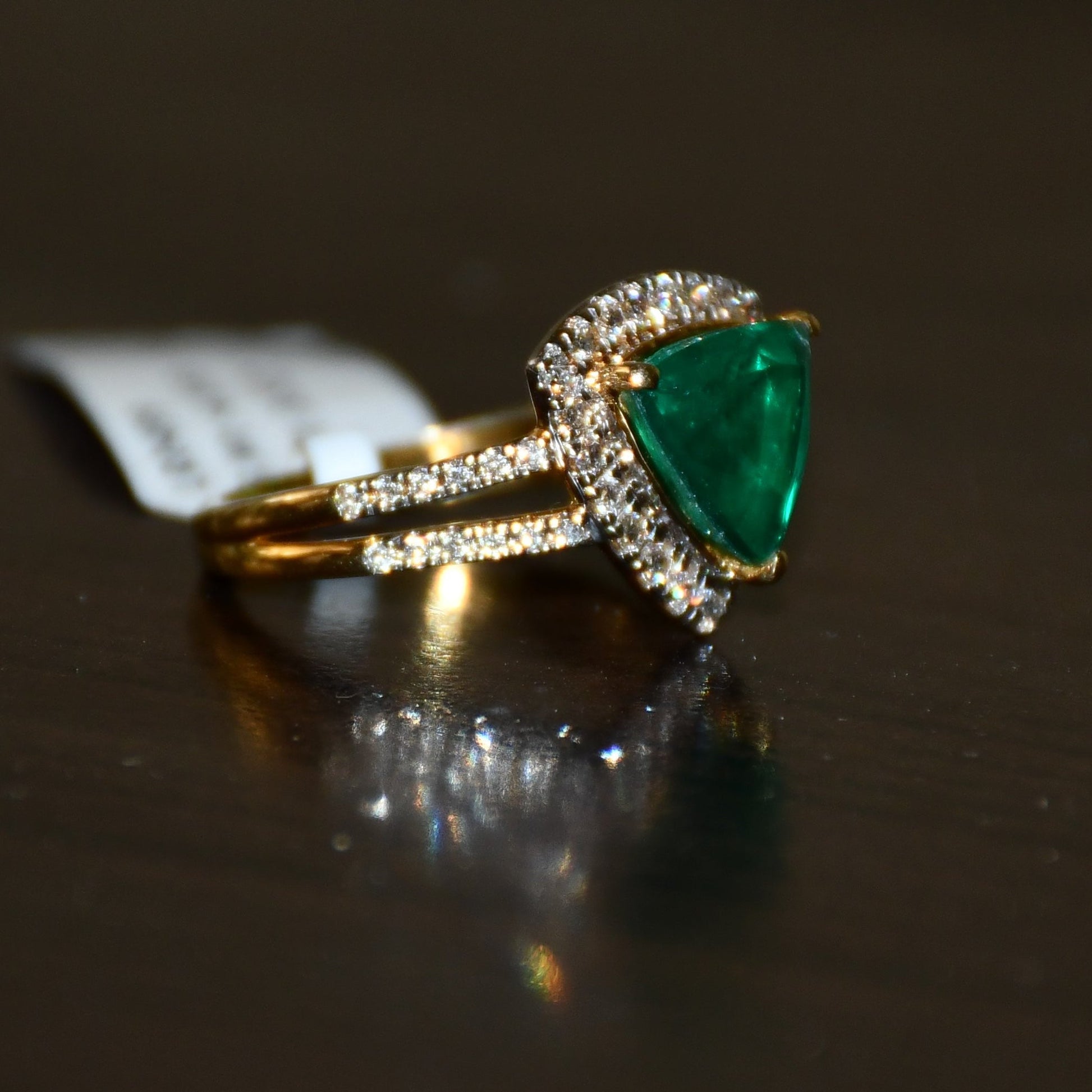 A green semi-precious stone ring with a 14KT gold band and brilliant cut diamonds on the top and bottom is displayed on a reflective surface.