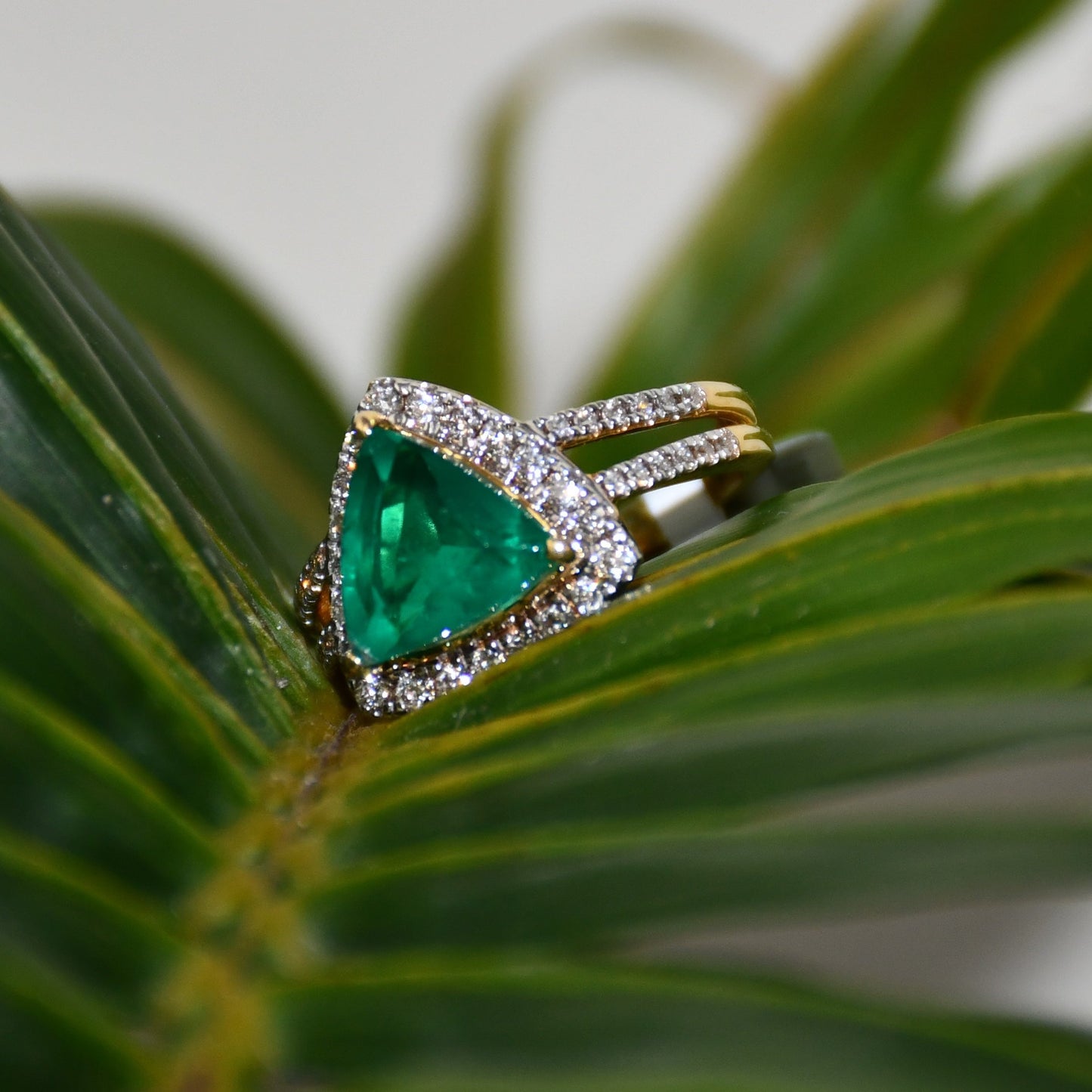 A green semi-precious stone ring with a 14KT gold band and brilliant cut diamonds on the top and bottom is displayed on a green leaf.