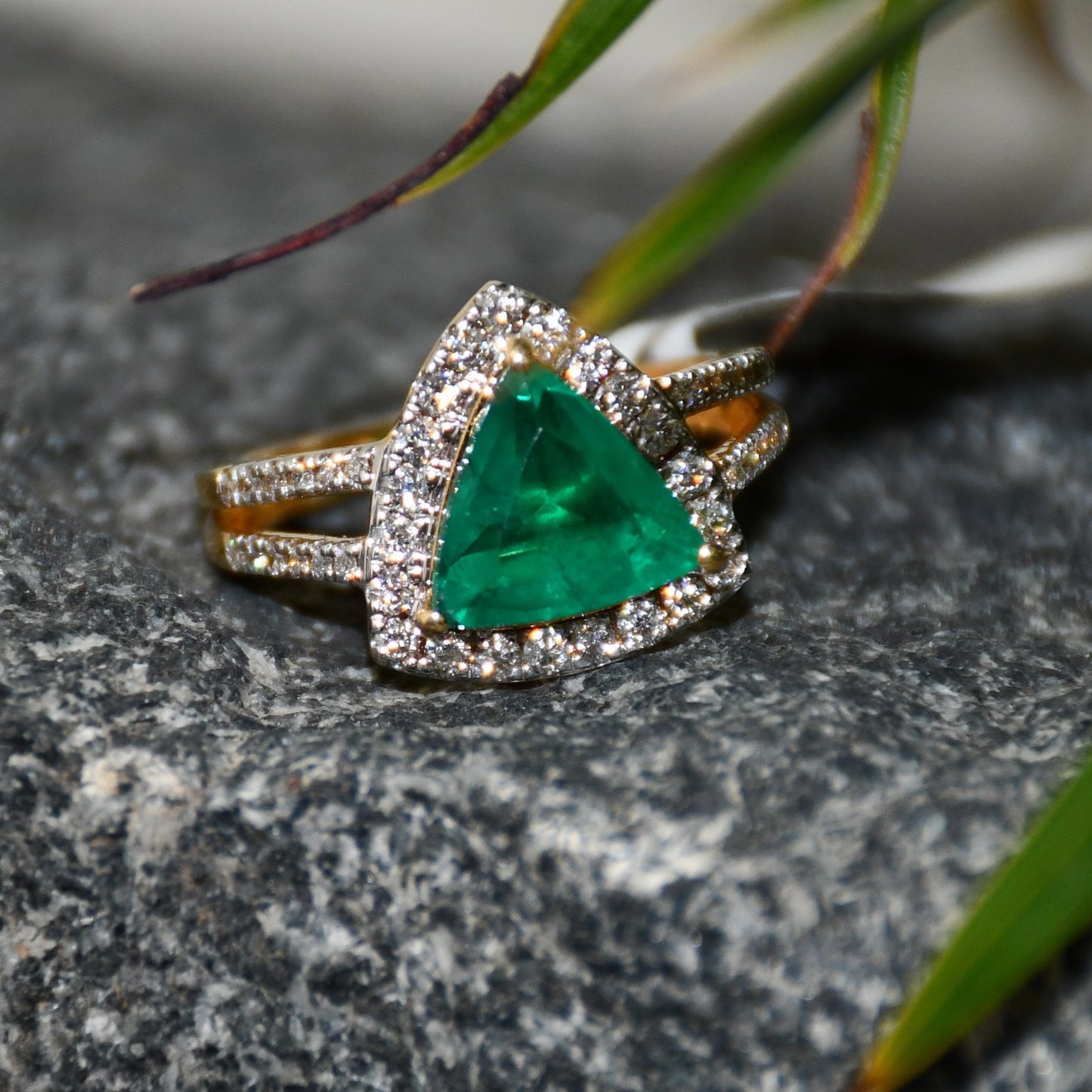 A green semi-precious stone ring with a 14KT gold band and brilliant cut diamonds on the top and bottom is displayed on a rough & textured surface.
