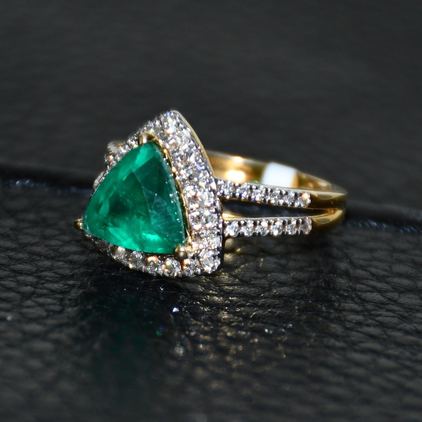 A green semi-precious stone ring with a 14KT gold band and brilliant cut diamonds on the top and bottom is displayed on a black leathered surface.