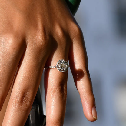A person's hand holding a diamond ring in its finger.