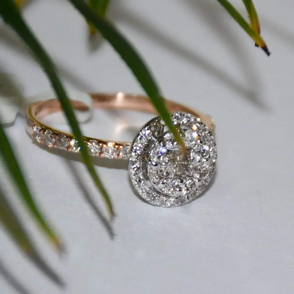 A diamond ring is displayed on a reflective surface with a leafy background.