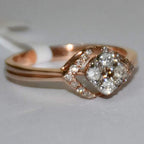A gold ring with a central diamond surrounded by smaller diamonds set in a solid gold band is displayed on a white surface.