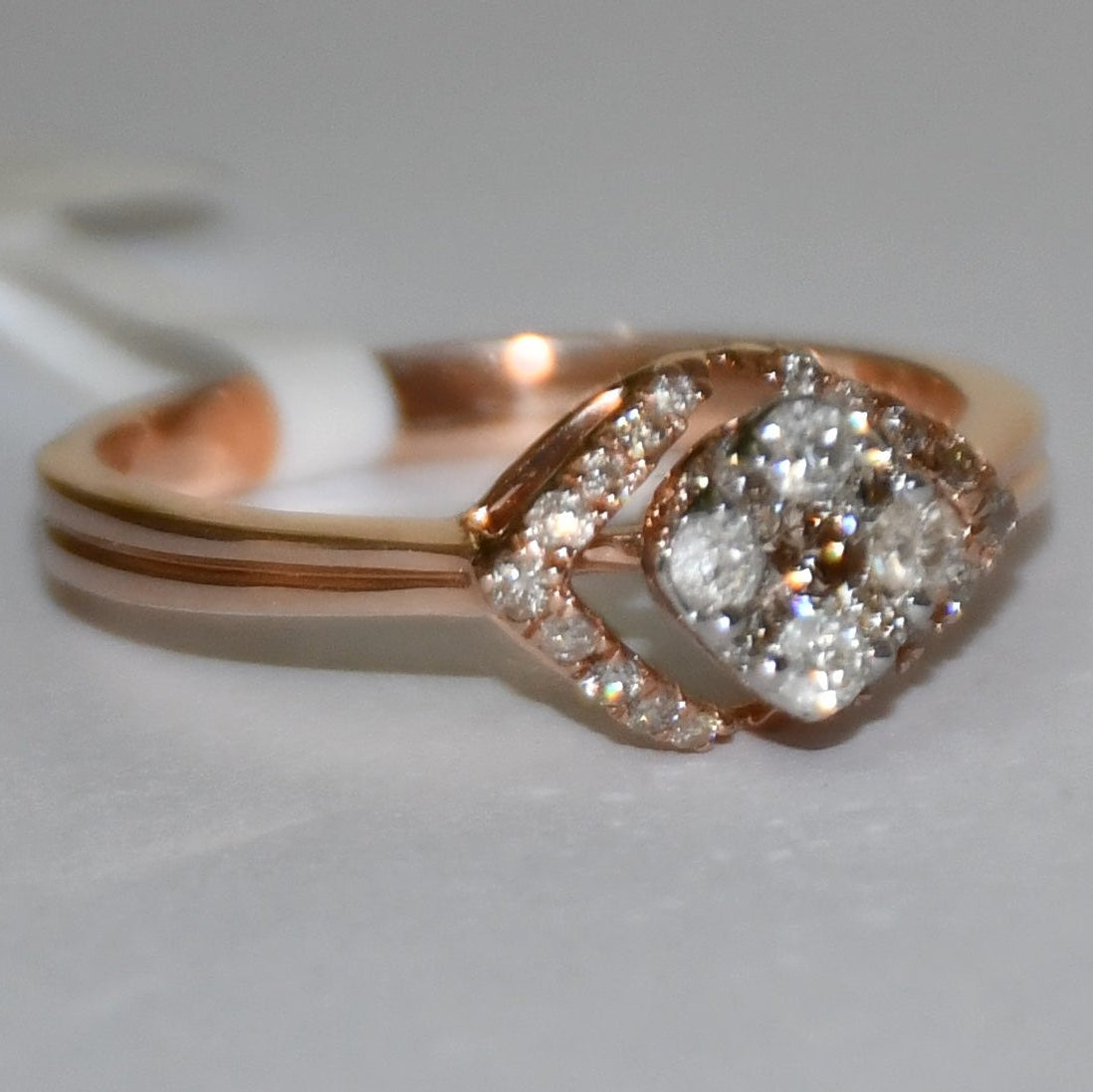 A gold ring with a central diamond surrounded by smaller diamonds set in a solid gold band is displayed on a white surface.