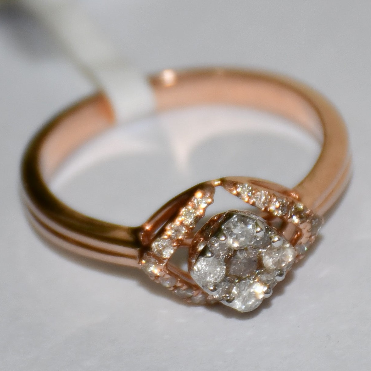 A gold ring with a central diamond surrounded by smaller diamonds set in a solid gold band is displayed on a white surface.