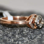 A gold ring with a central diamond surrounded by smaller diamonds set in a solid gold band is displayed on a rough & textured surface.