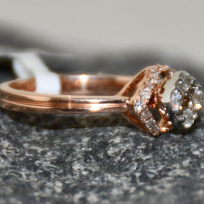 A gold ring with a central diamond surrounded by smaller diamonds set in a solid gold band is displayed on a rough & textured surface.