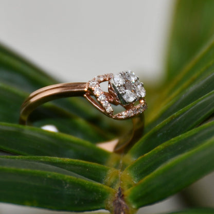 A gold ring with a central diamond surrounded by smaller diamonds set in a solid gold band is displayed on a leafy surface.