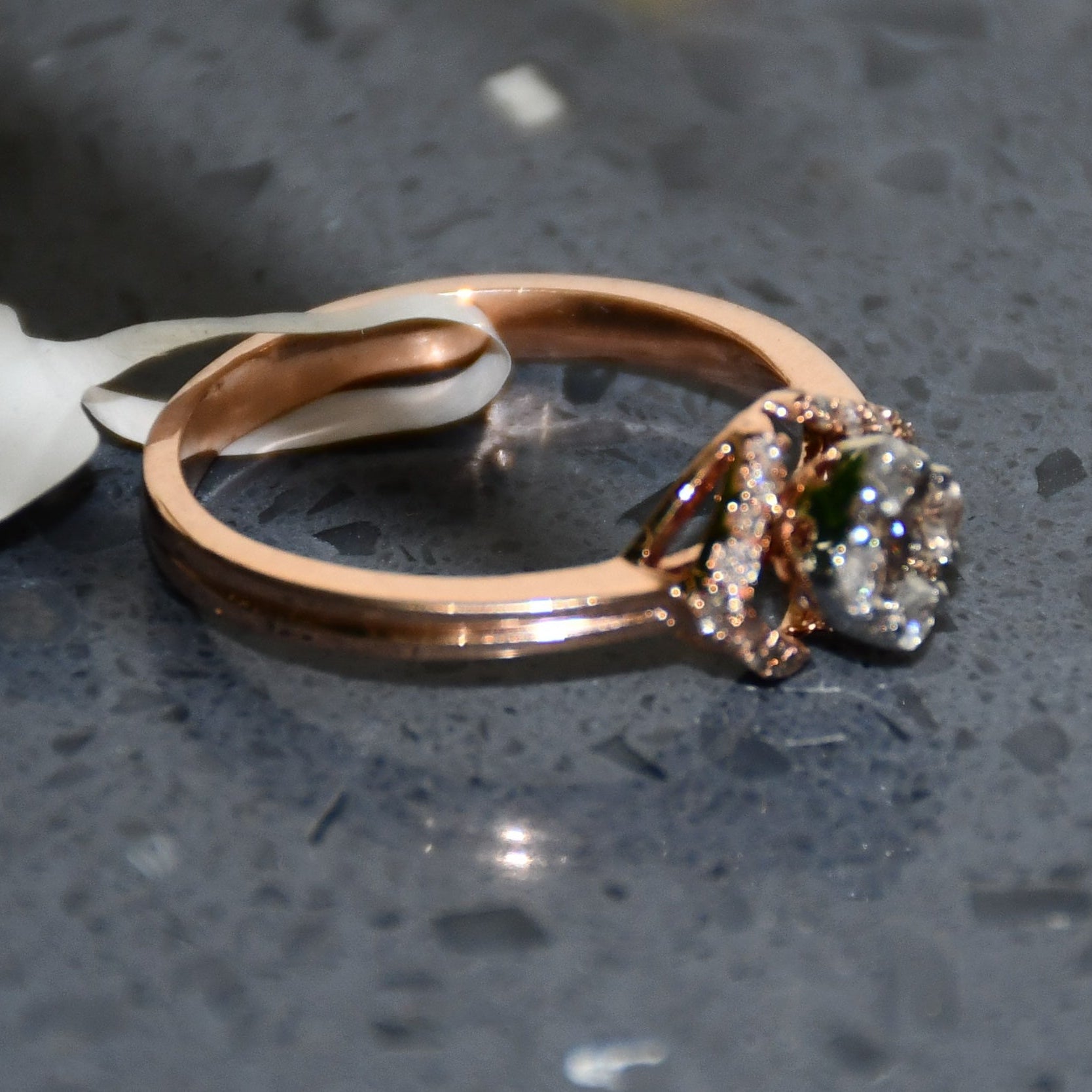 A gold ring with a central diamond surrounded by smaller diamonds set in a solid gold band is displayed on a grey smooth surface.