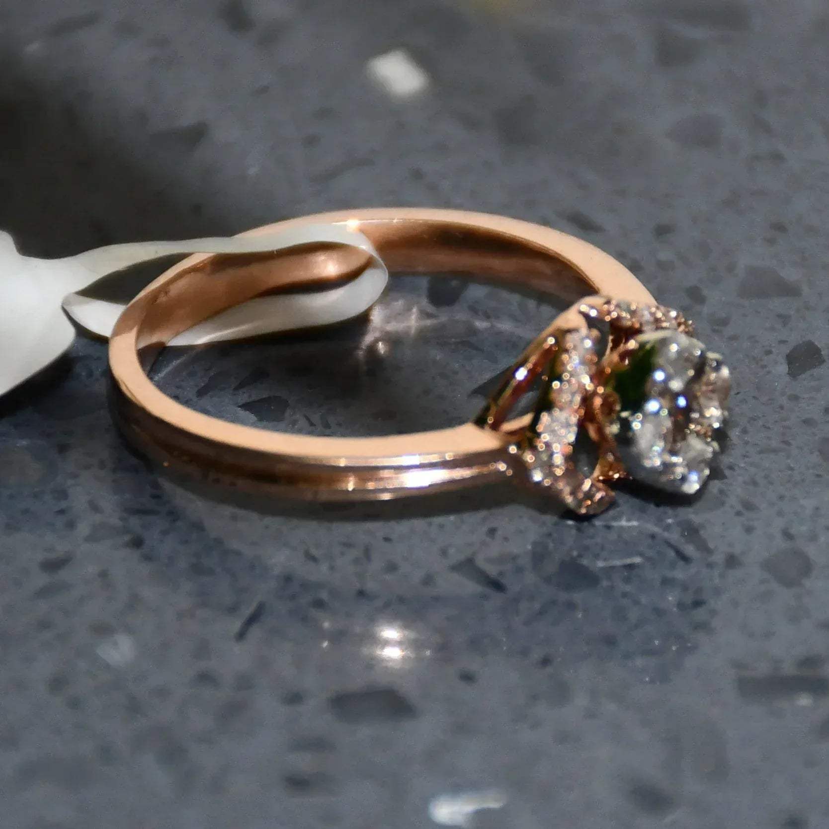 A gold ring with a central diamond surrounded by smaller diamonds set in a solid gold band is displayed on a grey smooth surface.